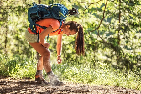 A woman applies bug spray in the woods to protect against ticks.